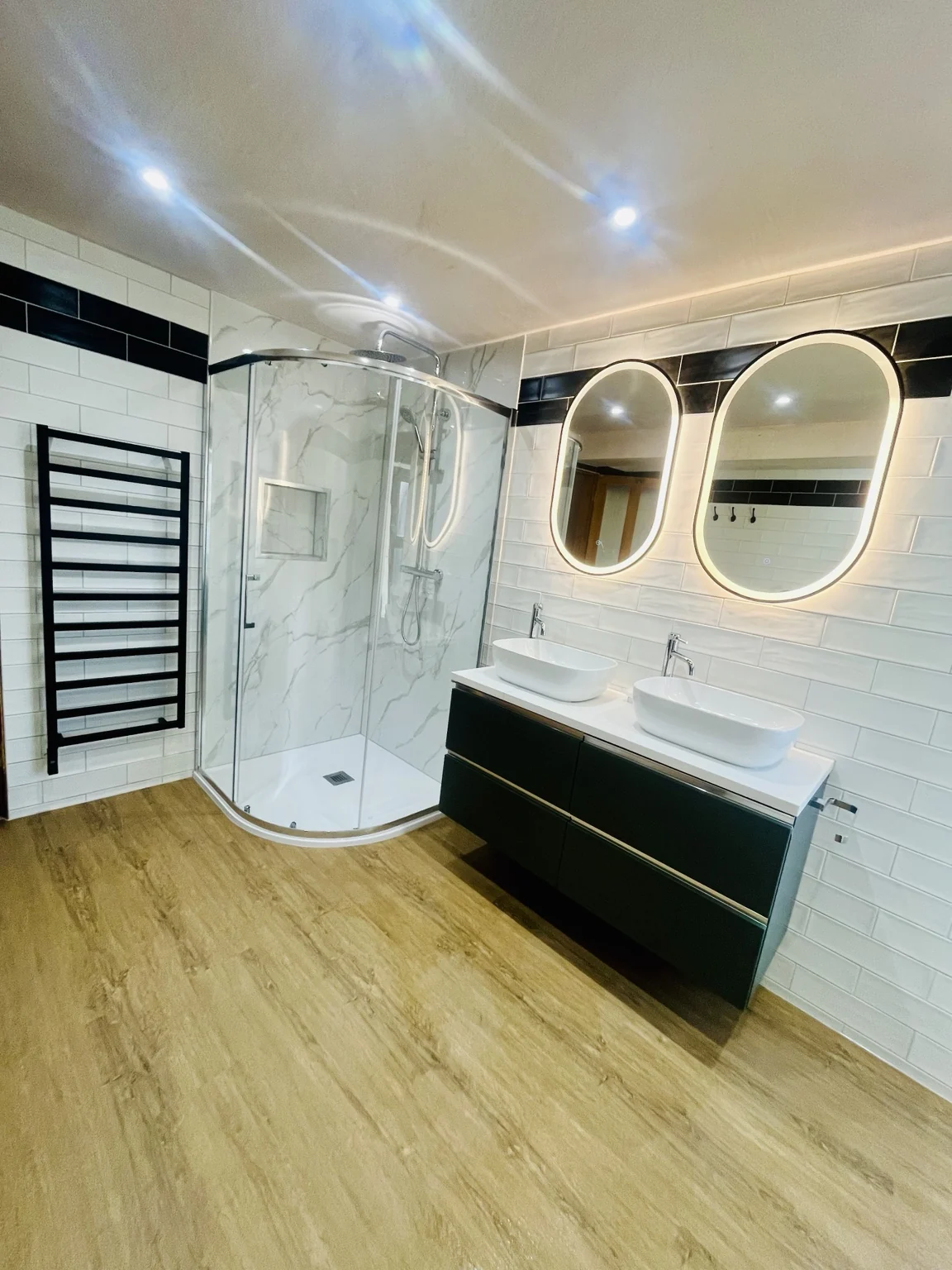 Black double vanity, illuminated mirrors and curved shower — completed DDI bathroom